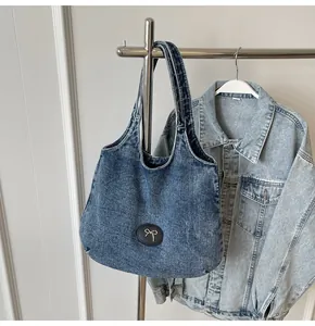 Detail view of denim tote bag featuring a leather patch with a silver bow logo