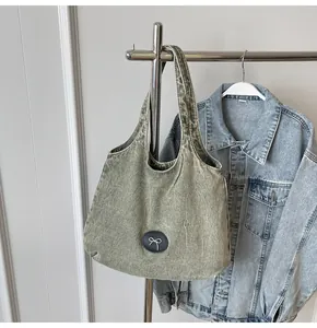 Detail of vintage washed denim tote bag showing grey-green texture and bow logo patch