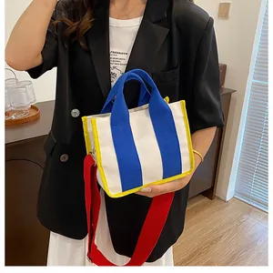 Detail der Canvas-Handtasche im Color-Block-Design mit rotem Gurt und Tragegriff am Model