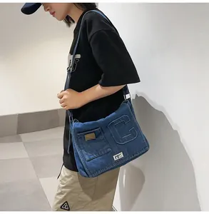 Detail of blue denim crossbody bag with letter C patch worn by a model in casual style