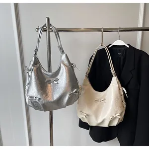 Close-up of silver and cream hobo bags featuring 3D bows and pleated leather texture