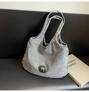Detail of washed grey denim tote bag featuring golden metal bow and leather patch