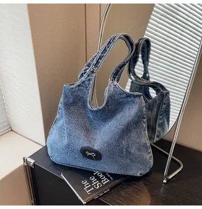 Detail of blue denim tote bag with leather bow buckle accent on black surface