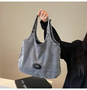 Detail of grey washed denim tote bag featuring silver bow accent and oval leather patch