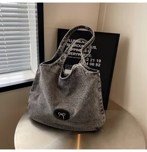 Detail of grey washed denim tote bag with metal bow leather patch on a metal table