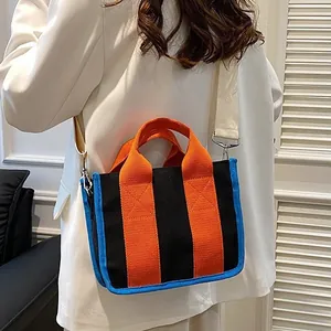 Driekleurige canvas handtas met afneembare brede riem gedragen door een vrouwelijk model