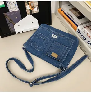 Detail of dark blue denim messenger bag featuring large 'C' patch and metallic twist lock
