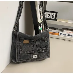 Detail of dark gray washed denim shoulder bag featuring a large C letter and metal clasp