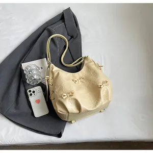 Detail of cream yellow pleated tote bag featuring bow accents and drawstring side texture