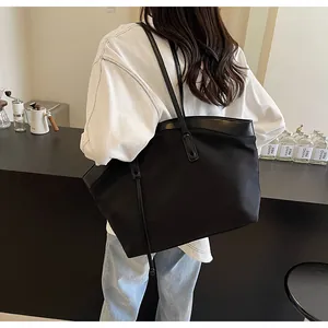 Model wearing a large black nylon tote bag with leather trim in a cozy cafe setting