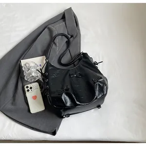 Detail of black crescent tote bag with glossy texture and elegant bow embellishments