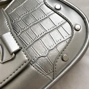 Close-up of silver crocodile embossed handbag with metal studs and engraved logo text