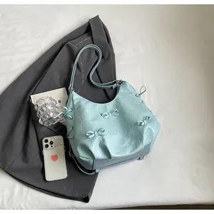 Detail of light blue tote bag with ribbon bows and pleated leather texture on white backdrop
