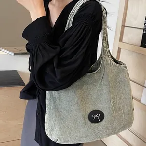 Chic oversized denim tote bag with metallic bow emblem and washed vintage finish