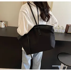 Model wearing a large black nylon tote bag with leather straps in a stylish cafe setting