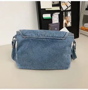 Detailed shot of light blue washed denim messenger bag with wide strap and silver buckle