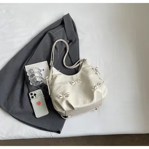 Detail of white pleated moon bag featuring four delicate decorative bows and soft texture