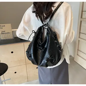 Detail of black pleated tote bag with bow accent and eyelet lacing on model's back