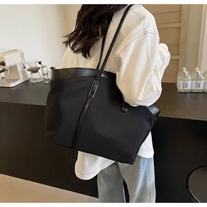 Detail of black large capacity tote bag with leather trim worn in a cafe setting