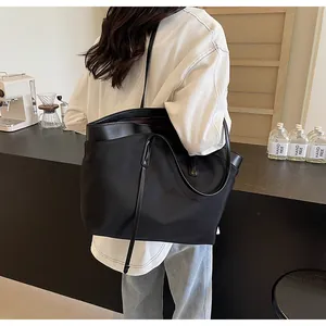 Detailed view of a black large capacity nylon tote bag worn by a model in a cafe setting