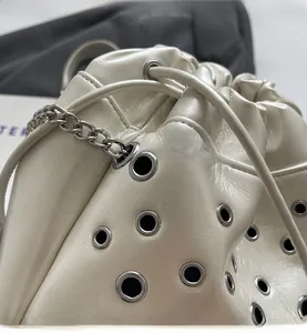 Détail du sac seau crème montrant les oeillets métalliques et la bandoulière chaîne
