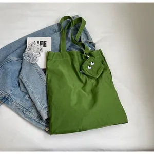 Detail view of grass green nylon tote bag with embroidered eye mini pouch and wide strap