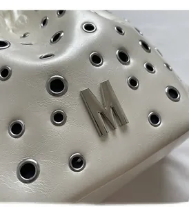 Détail du sac seau en cuir crème avec œillets argentés et plaque logo M en métal