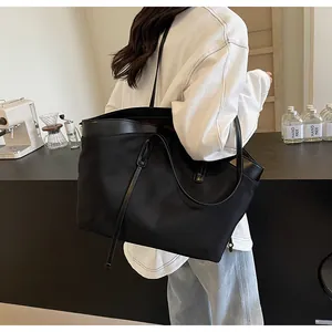 Lifestyle view of large black nylon tote bag on shoulder in a minimalist cafe setting