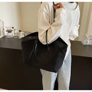 Detail of a large black nylon tote bag showing leather trim and dual strap versatility