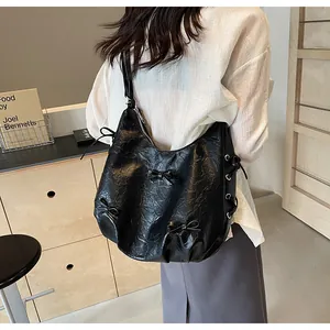 Detail of black hobo bag showing crinkled texture, ribbon bows, and side drawstring design