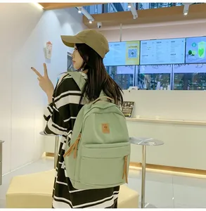 Rear view of a light green casual backpack showing adjustable straps and leather logo detail