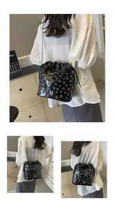 Détail du sac seau noir brillant avec œillets argentés, logo M en métal et chaîne