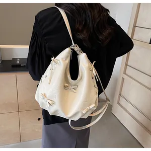 Detail of cream hobo bag with ribbon bows shown on model in a minimalist setting