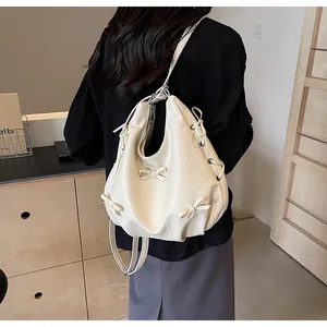 Detail of cream pleated backpack with bows and silver eyelets shown on a model back