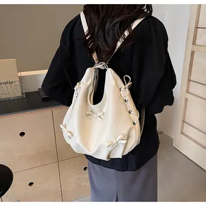 Detail of cream white PU leather backpack with bow accents shown on model's shoulder