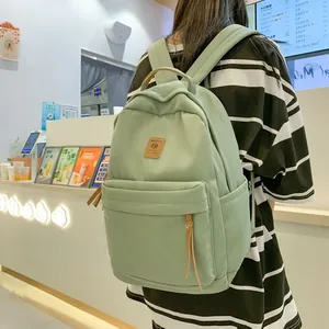 Student backpack in light green canvas featuring a large main compartment and leather patch