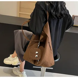 Detail view of brown embroidered tote bag with cute monster eye charm on a fashion model