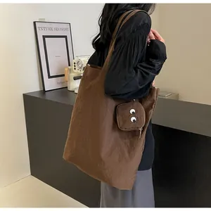 Macro detail of dark brown foldable tote bag with cartoon eye mini pouch and embroidery