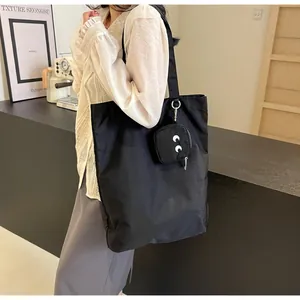 Detail view of a black oversized tote bag with a cartoon eye embroidered mini pouch