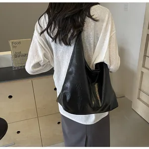Gros plan d'un sac hobo noir à texture froissée brillante porté par un mannequin de côté