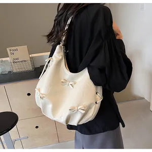 Creamy white leather hobo bag with bow details and drawstring side being worn