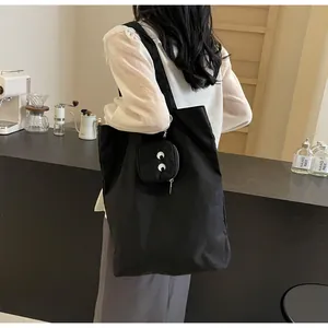 Detail of black nylon tote bag with small monster eye pouch accessory on a model