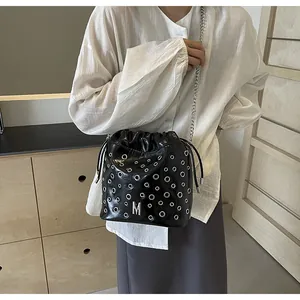 Détail du sac seau noir brillant avec œillets argentés, logo M et bandoulière chaîne