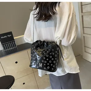 Détail du sac seau en cuir noir avec œillets argentés et logo lettre M en métal