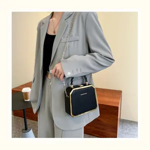 Détail d'un sac à bandoulière noir avec chaîne dorée dans un décor de rue chic