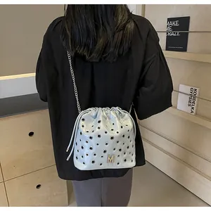 Détail d'un sac seau bleu clair avec œillets métalliques et bandoulière chaîne