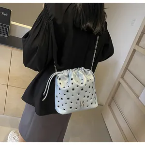 Détail du sac seau bleu clair avec œillets argentés et logo M sur bandoulière