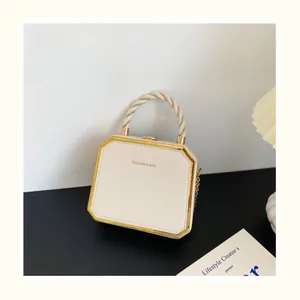 Détail du sac carré crème avec bordure dorée, poignée torsadée et bandoulière chaîne