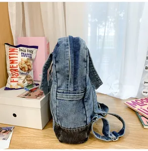Side view of denim backpack showing stitching details and durable wash fabric on a desk