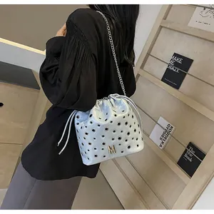 Détail du sac seau bleu clair avec œillets métalliques argentés et logo M doré sur la bandoulière